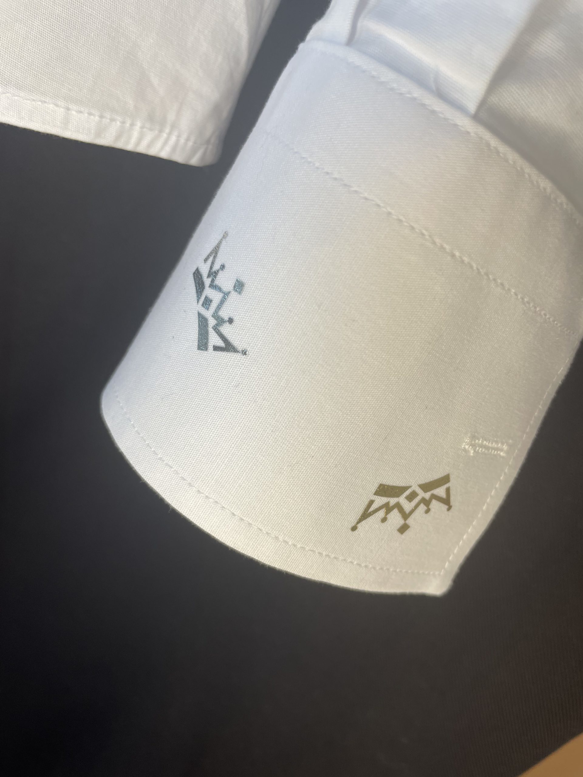 Zoom sur le poignet d’une chemise avec des petites couronnes or et argent